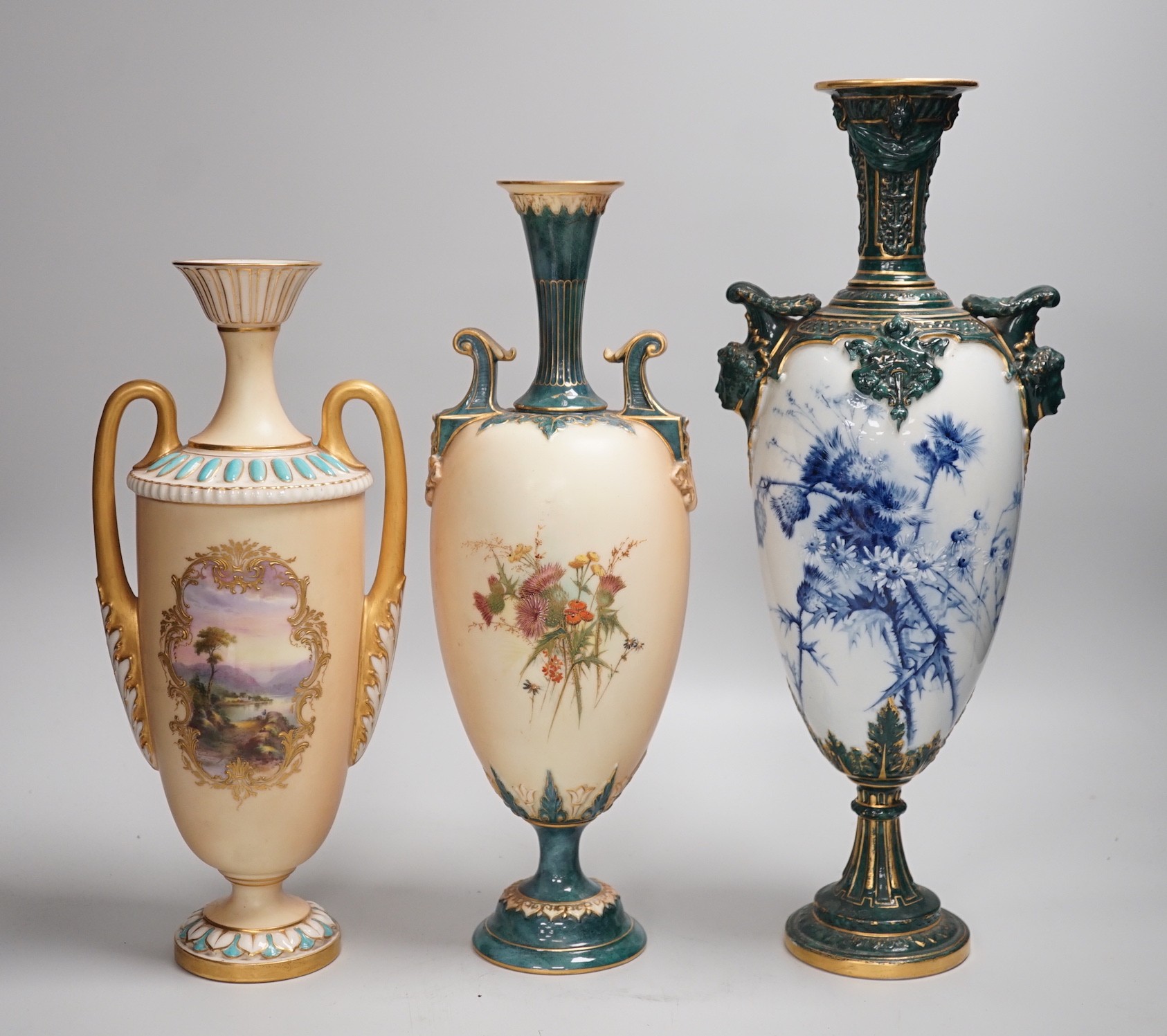 Three Royal Worcester pedestal vases, each of ovoid form and supported on circular pedestal feet, two are decorated with flowers and thistles, the other depicting a rural landscape within a gilt foliate C scroll cartouch